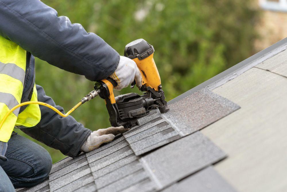 Roofer nailing replacement shingles after storm damage